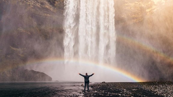 Mann bei Wasserfall mit Regenbogen - Credit: Erondu/unsplash
